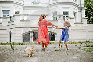 Mom and daughter in bright dresses are spinning and having fun on summer day in park. Positive.