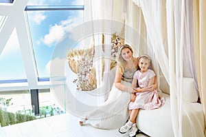 mom and daughter Caucasians with blond hair sitting on the sofa. Modern bright interior