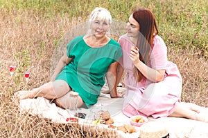 Mom and daughter celebrate mother`s day on a summer picnic. Beautiful adult and young women relax in nature with food and drink