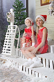 Mom and daughter in Christmas costumes are sitting under snow