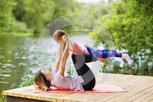 Mom and daughter do yoga on a wooden bridge on a warm sunny morning near the river