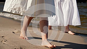 Mom and daughter in dresses walking along the beach, close-up of legs