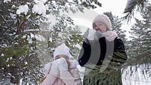 Mom and daughter drinking hot tea from cup in winter forest at frosty day