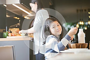 Mom and daughter eating Cereals with milk having breakfast in kitchen.