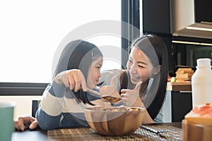 Mom and daughter eating Cereals with milk having breakfast in kitchen.