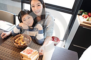 Mom and daughter eating Cereals with milk having breakfast in kitchen.