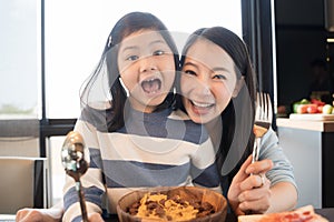 Mom and daughter eating Cereals with milk having breakfast in kitchen.