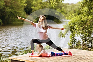 Mom and daughter are engaged in morning exercises on a wooden bridge near the river