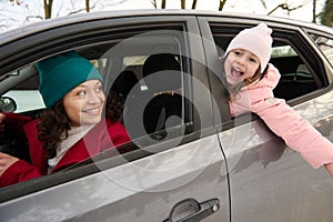 Mom and daughter enjoy winter trip by car, along snow covered nature. Family travel concept. Adorable little girl smiles cutely,