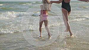 Mom and daughter flee along the beach to swim in the sea