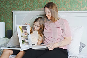 Mom and daughter flipping through a wedding photo book on the bed.