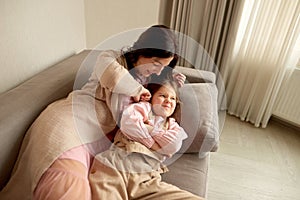 Mom and daughter fooling around at home. mom tickles daughter lie on sofa in house. daughter sulks at mom