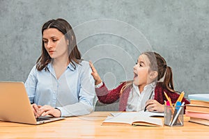 Mom and daughter on a gray background. During this mom works on a gray laptop. The girl calls her mother holding her