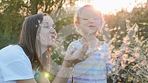 Mom and daughter having fun and blowing Dandelion seeds while relaxing at nature