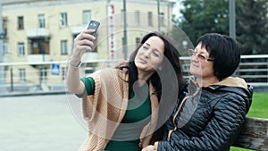 Mom and daughter are having fun together while making selfies on a smartphone. An adult woman depicts horns on a young