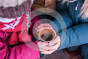 Mom and daughter hold a hot cup of coffee in their palms. Family on a walk together in winter