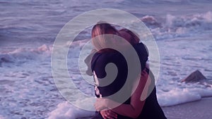 Mom and daughter hug, laugh, smile, against the backdrop of sea, big waves, foam, beach