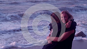 Mom and daughter hug, laugh, smile, against the backdrop of sea, big waves, foam, beach