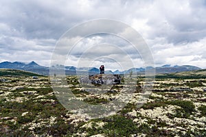 Mom and daughter hugging on a mountain top on a big rock with beautiful mountain view of Rondane national park in Norway.