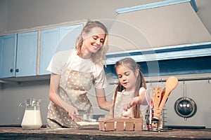 Mom and daughter in the kitchen cook Mafins. A daughter holds a chicken egg in her hand which will add to the flour