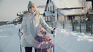 Mom and daughter look at the camera and smile before nordic walking in the suburbs in winter.