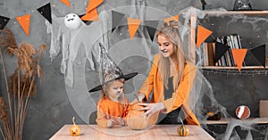Mom and daughter make a pumpkin jack-o-lantern for Halloween. Traditional autumn witch holiday at home family. October