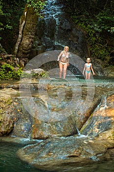 Mom and daughter on a mountain river under a waterfall in the jungle.Turkey.