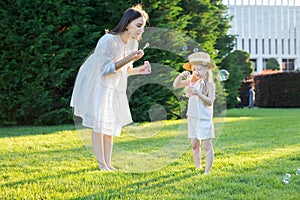 Mom and daughter in the park inflate soap bubbles. Have fun on a sunny summer day