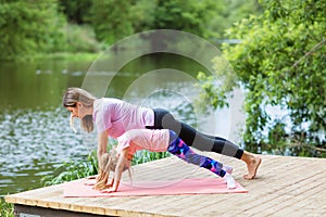 Mom and daughter perform a plank exercise on the river bank on a warm summer day