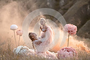 Mom and daughter in pink fairy-tale dresses play in a field surrounded by Big pink decorative flowers