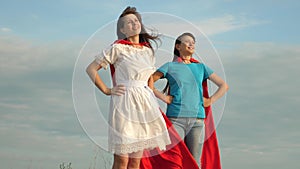 Mom and daughter play superheroes. two girls in red cloaks of superheroes stand against a blue sky, the wind inflates a