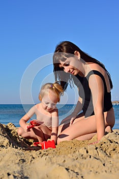 Mom and daughter are playing in the sand on the beach