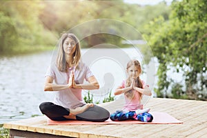 Mom and daughter practice yoga asanas on the river bank on a warm sunny day. Healthy lifestyle concept