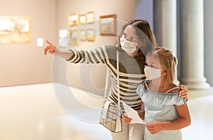 Mom and daughter in protective masks inspect the exhibits of museum