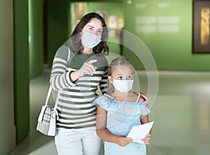 Mom and daughter in protective masks inspect the exhibits of museum