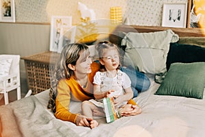 Mom and daughter are reading a book and smiling, sitting at home on the bed. New Year, Christmas, family, time together