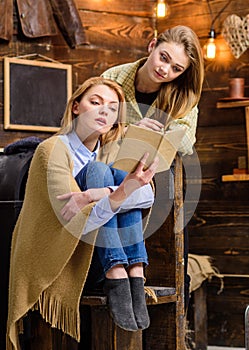 Mom and daughter reading together. Woman wrapped in woolen blanket holding book. Mother helping teenage child with