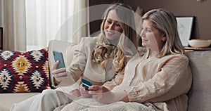 Mom and daughter relax on the couch. The young girl helps the senior to shop online, they transcribe the credit card