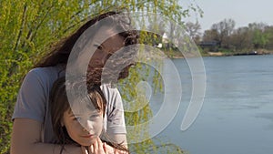 Mom and daughter on the river bank. Woman with child on a sunny day by the water. Happy family in nature.