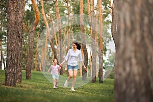 Mom and daughter are running in the forest. The sisters are playing hide and seek in the forest. Mother`s day, women`s holiday