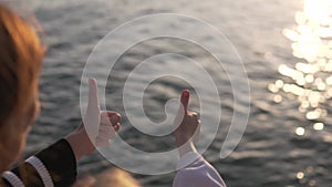 Mom and daughter show a clas gesture with their hand against the background of the sunset in the sea