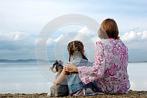 Mom and daughter sit embracing on the lake and look at the water