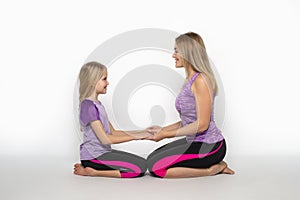 Mom and daughter sit on the floor holding each other`s hands with love  against white background in studio