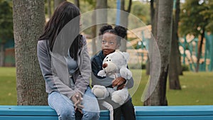 Mom and daughter sitting on bench child holding teddy bear little girl showing five fingers african american family