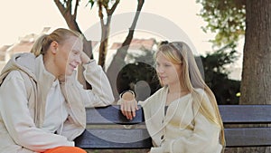 Mom and daughter are sitting on a bench in the park on an autumn day