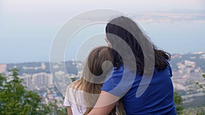 Mom and daughter sitting on mountain edge with amazing sea and city landscape. Happy mother and girl teenager admiring