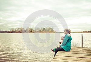 Mom and daughter are sitting on the pier at sunset