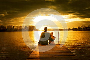 Mom and daughter are sitting on the pier at sunset