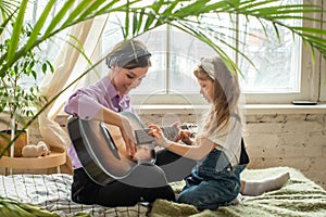 mom and daughter on the sofa, playing the guitar. a woman and a girl compose music, songs togethe