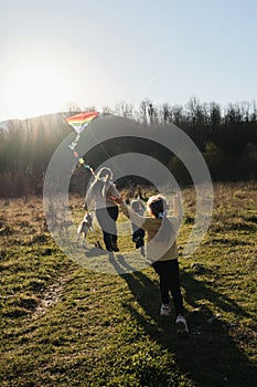 Mom with daughter and son and white half-breed dog. Happy family runs around field at sunset and plays with kite. Launch